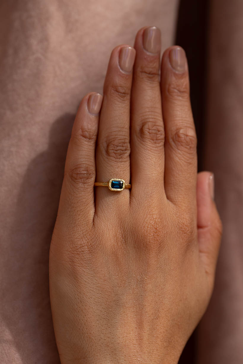 Hand wearing the Arbor Ring in recycled gold with an emerald-cut Australian sapphire