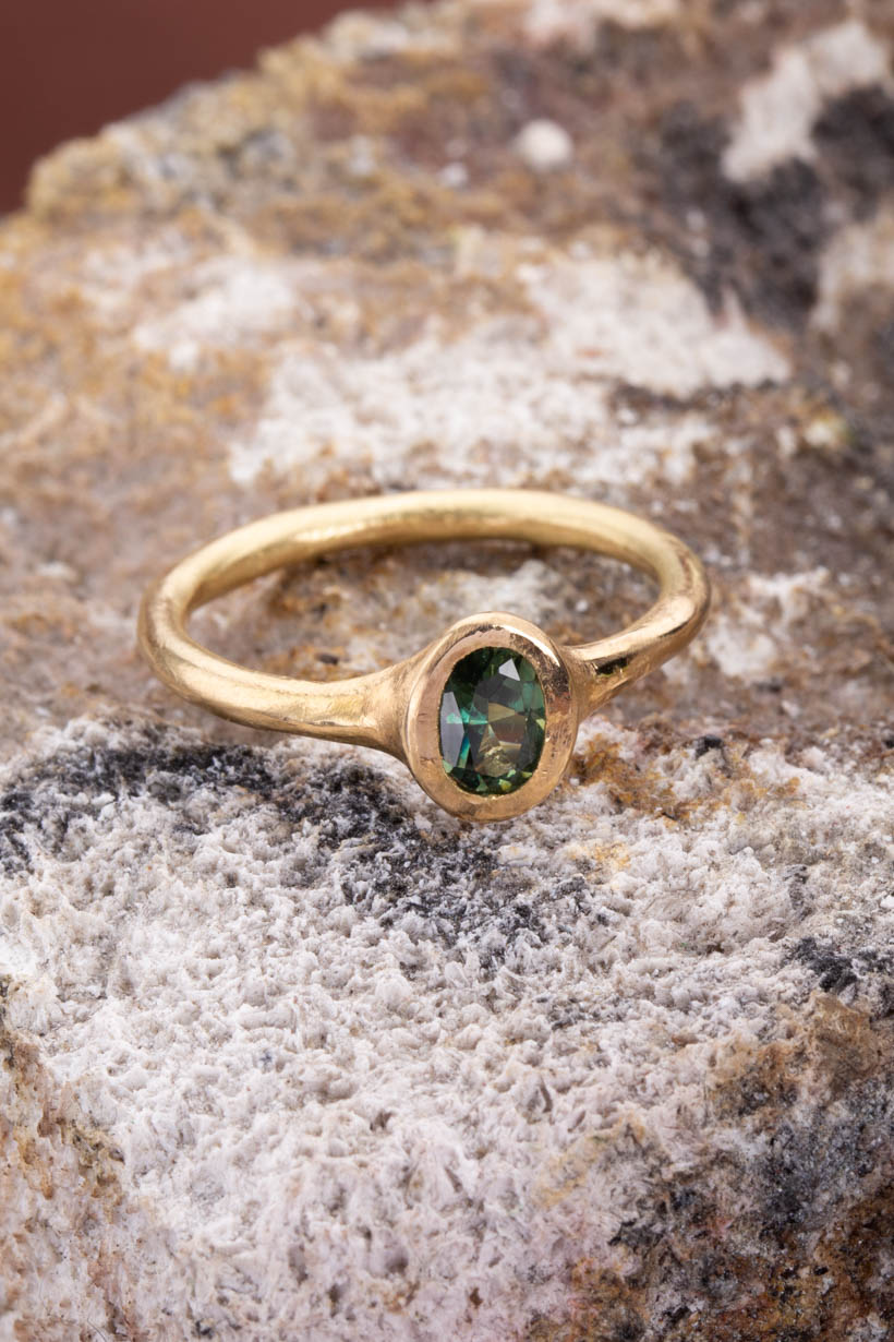 Gold ring with a green gemstone on a textured stone surface