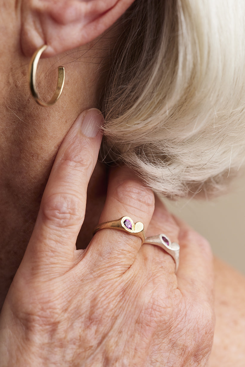 Close-up of a person wearing gold hoop earrings and rings with heart-shaped stones.