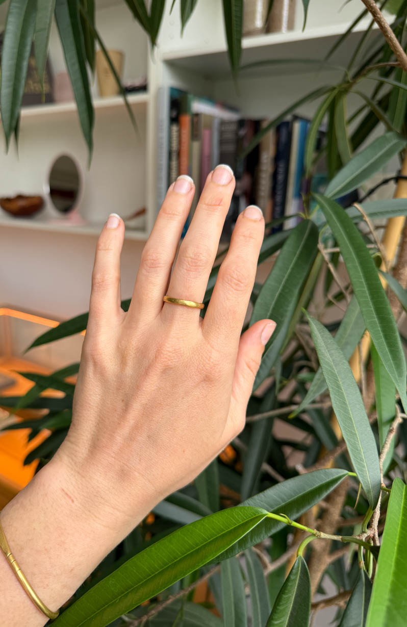 Hand wearing a gold ring with green leaves in the foreground