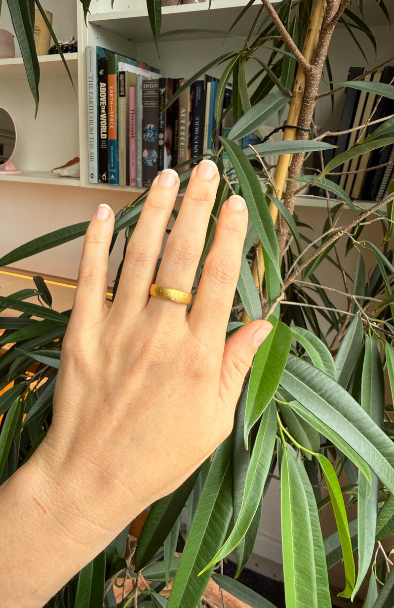Hand with a gold ring on a plant with a bookshelf in the background