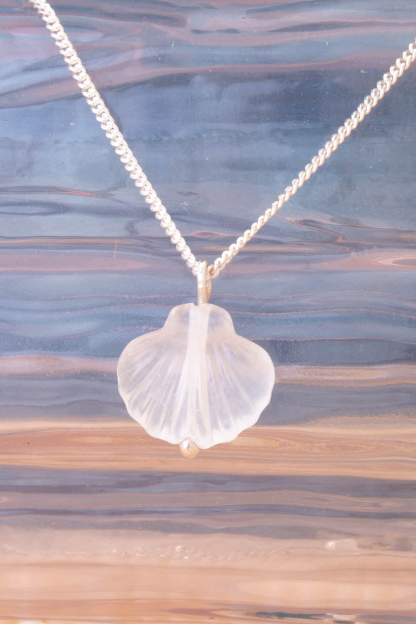 Shell pendant necklace on a chain against a water background