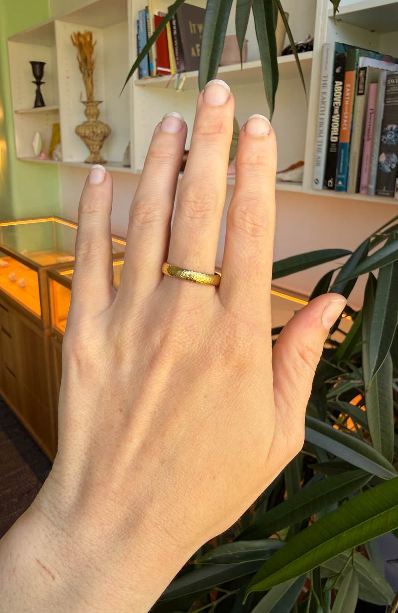 Moraine ring, 4mm wide gold band with dappled textured on hand.
