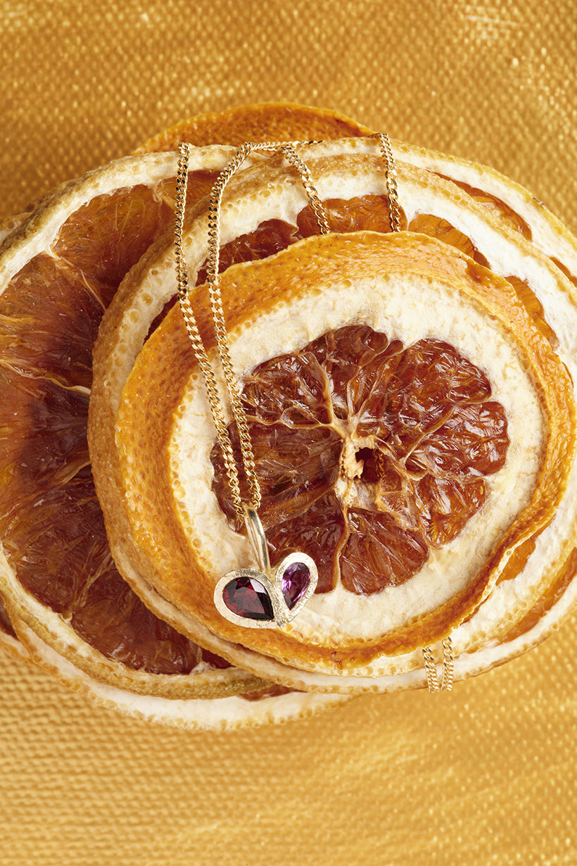 Necklace with a heart pendant on dried orange slices against a gold background