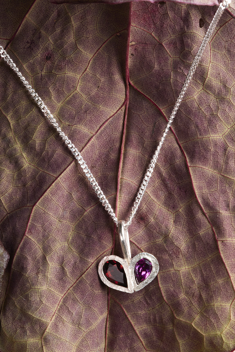 Silver necklace with a heart-shaped pendant featuring a purple gemstone on a leaf background