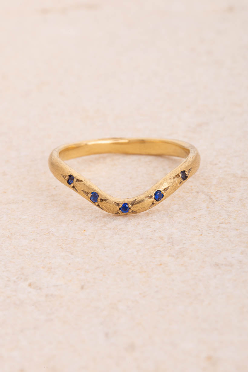 Curved Rosette wedding band with five ethically sourced blue Australian sapphires in rosette settings, handmade in Melbourne from recycled gold, front view on limestone