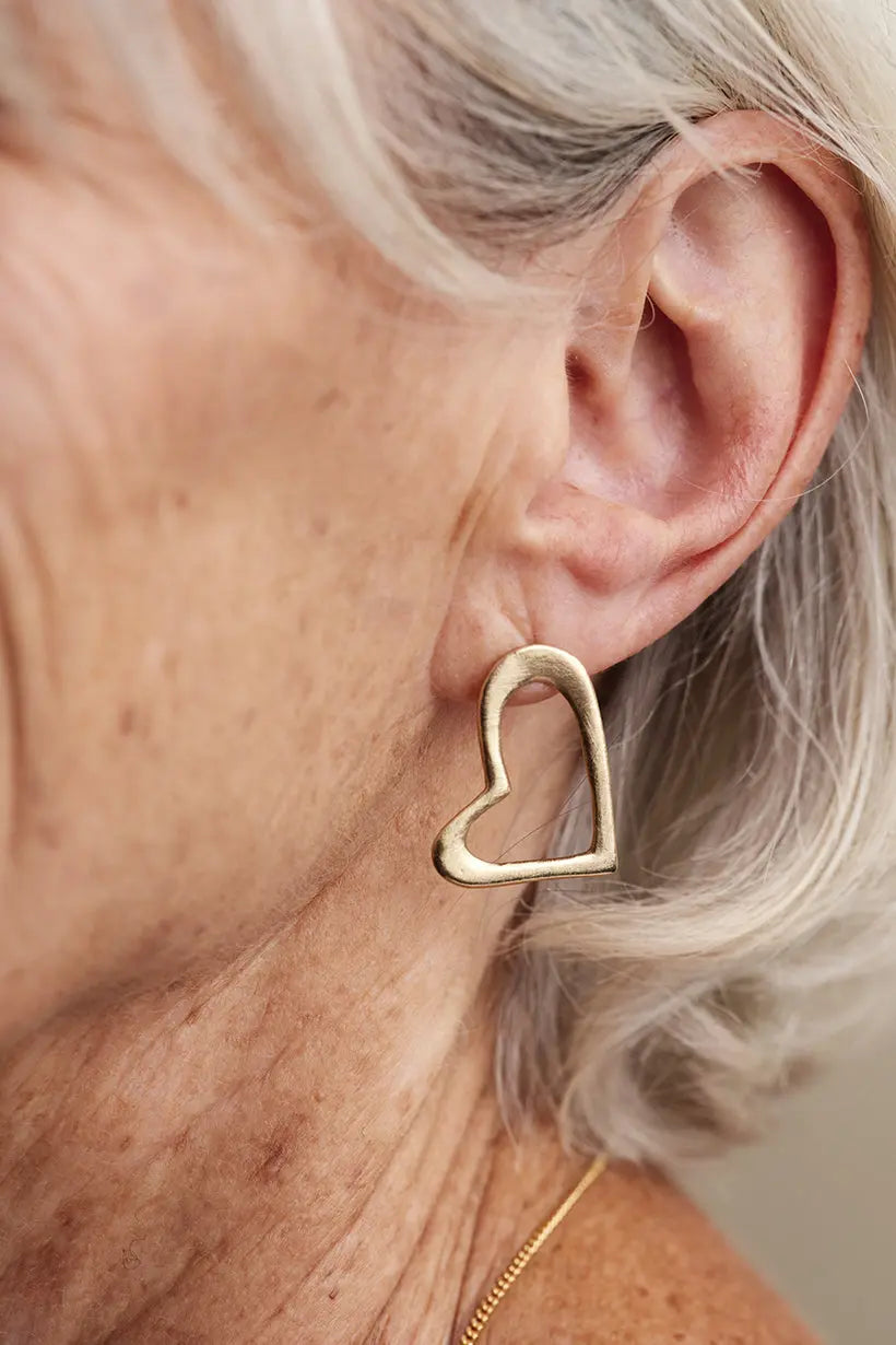Gold Heartline Earrings worn close to the ear – delicate open-heart stud earrings made from recycled gold, part of the Petal Hearts Collection