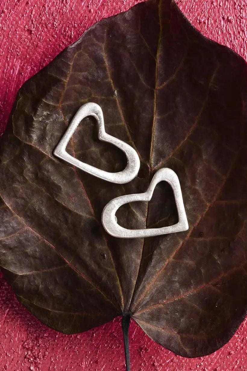 Sterling silver Heartline Earrings resting on a heart-shaped leaf – sculptural earrings inspired by nature, made in Australia from recycled silver