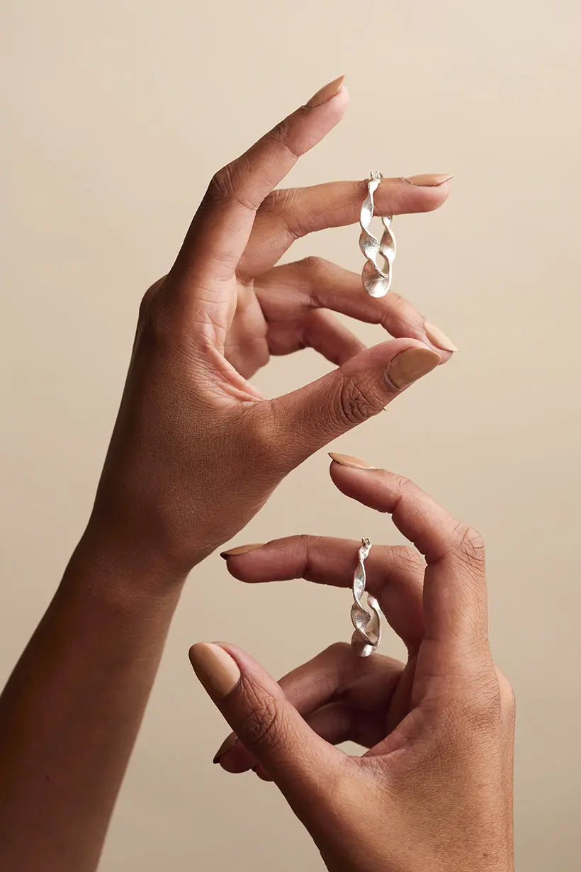 Hands holding a pair of large recycled silver hoop earrings with sculptural curves and a soft, textural finish, handmade in Melbourne.