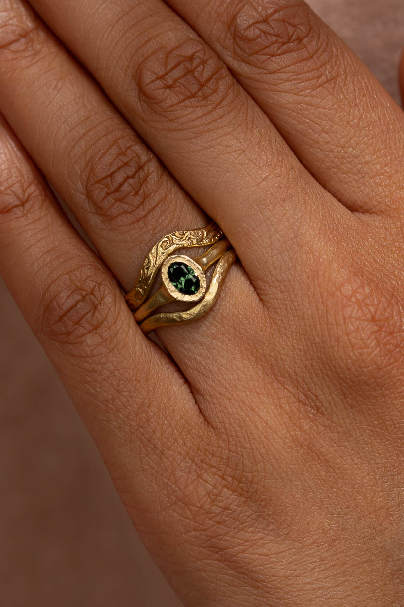 Close-up of the Bower ring on the hand, its green Australian sapphire framed by a thick textured bezel, with the Breeze and Whisper curved bands nestled on either side