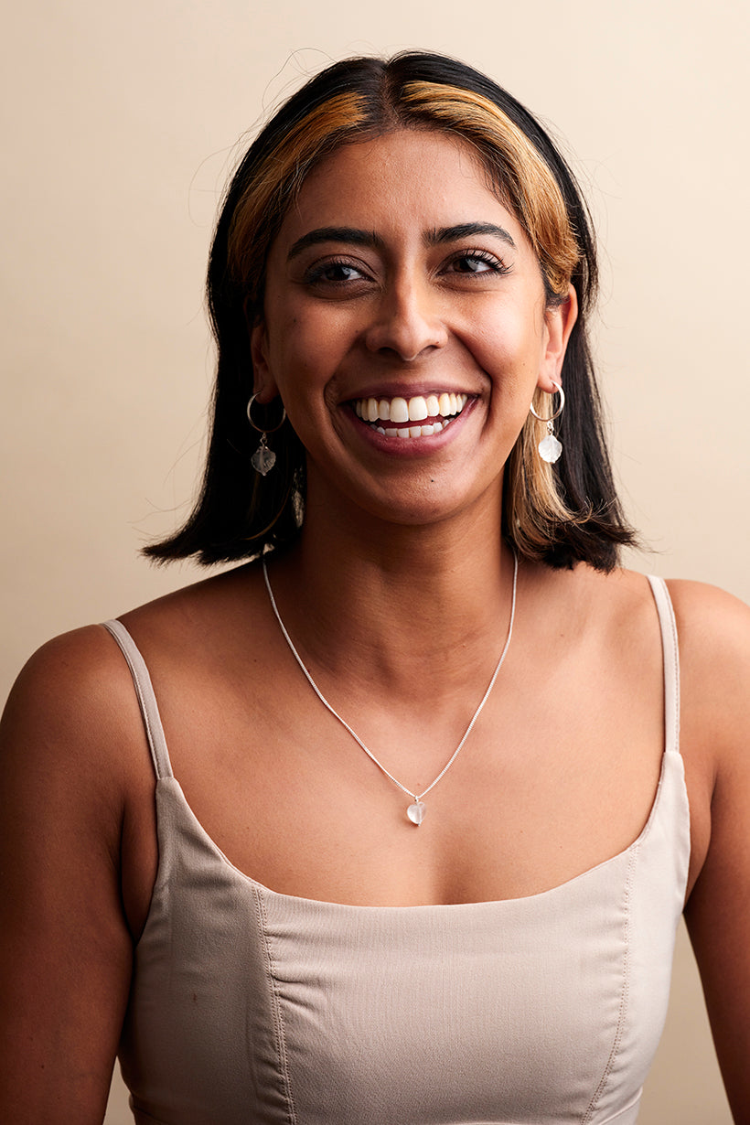 Model wearing glass heart necklace and seashore shell glass shell hoop earrings