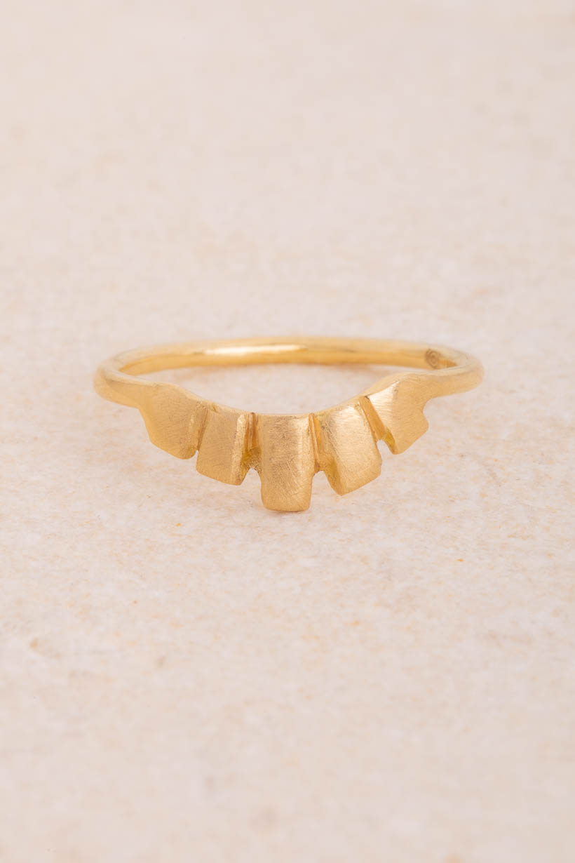 Keystone curved wedding band, an arch of hand-sculpted recycled gold tiles rising to a central keystone, made to nestle beside an engagement ring, handmade in Melbourne, front view on limestone