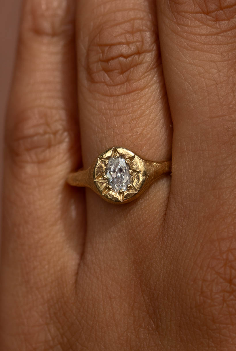 Monet’s Garden low-profile oval diamond engagement ring worn on the hand, a signet-style solitaire handmade in Melbourne from textured recycled gold, made to stack with a wedding band