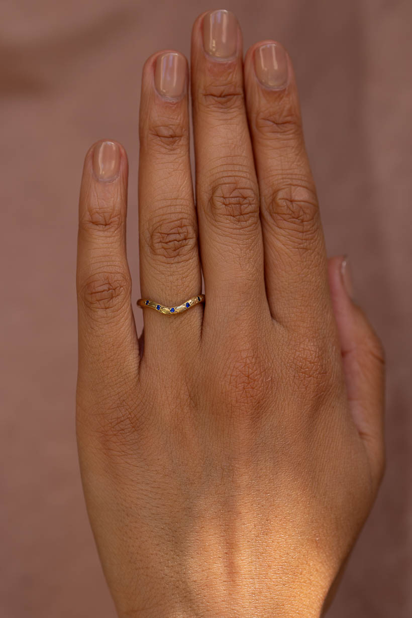 Curved Rosette wedding band with five blue Australian sapphires in a rosette setting, worn on the hand in recycled gold
