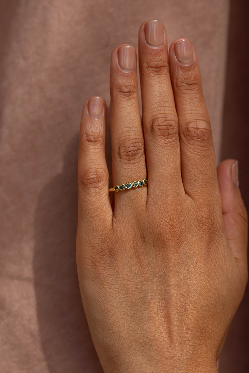 Gumnut wedding band with teal green Australian sapphires worn on the hand, a textured bezel set gemstone wedding ring by Ada Hodgson