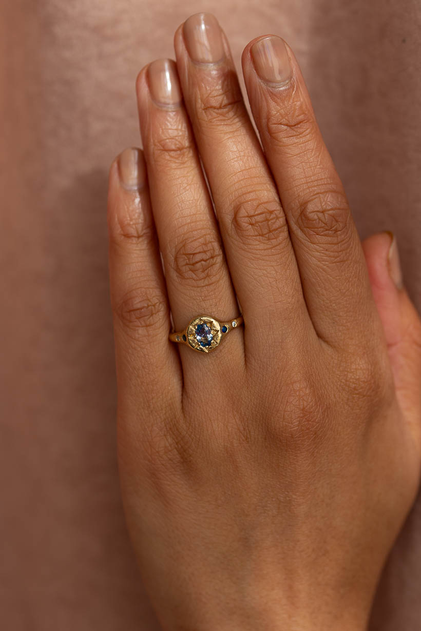 Monet's Garden Ring with light blue Ceylon sapphire, dark blue Australian sapphires and natural white diamonds in recycled yellow gold. Signet style engagement ring worn on model.