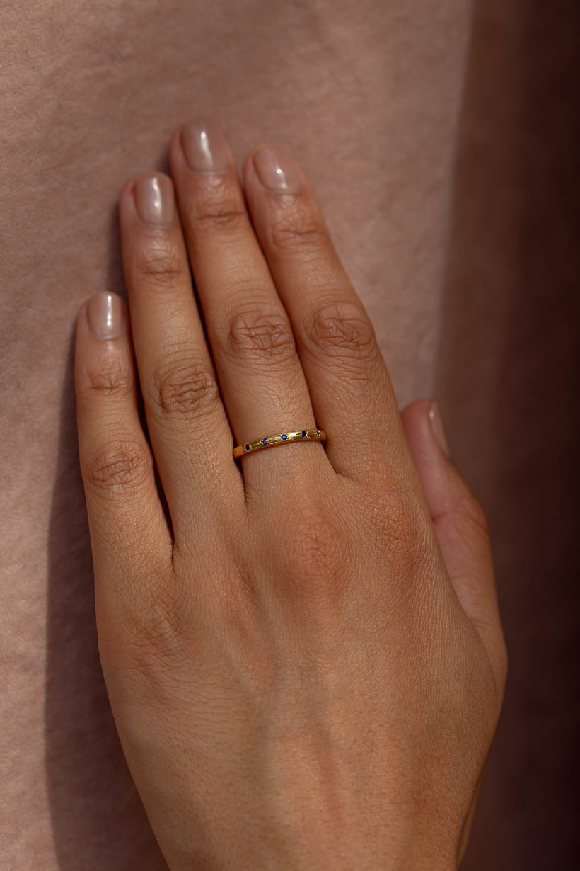The Rosette ring with five deep blue Australian sapphires worn on hand, a flower-set gemstone wedding band in recycled gold