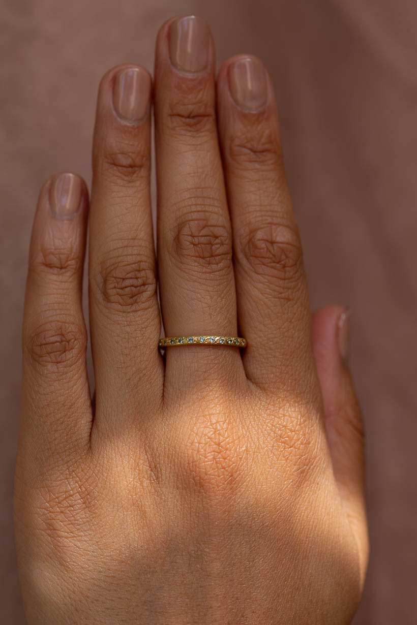 The Rosette ring with light green Australian sapphires worn on hand, a flower-set gemstone wedding band in recycled gold