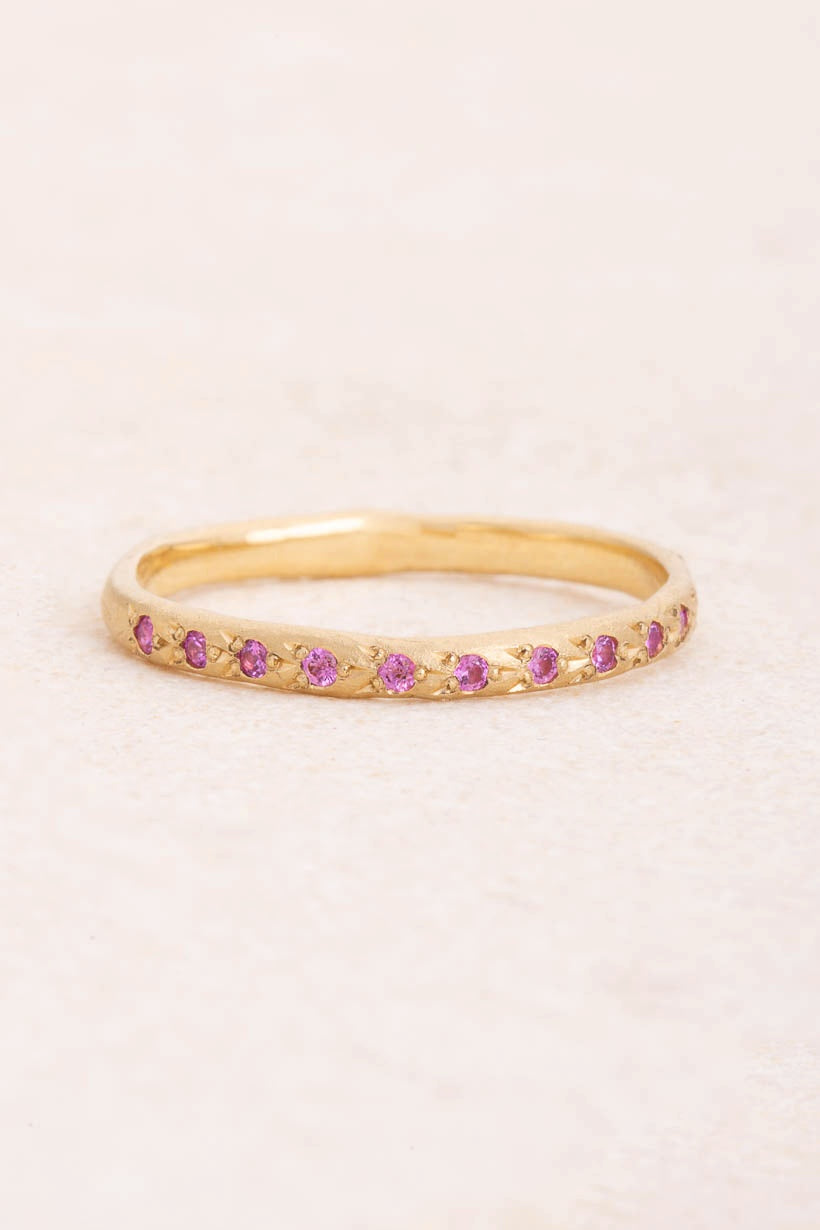Flat lay of the Rosette ring with eleven flower-set pink sapphires in textured recycled yellow gold