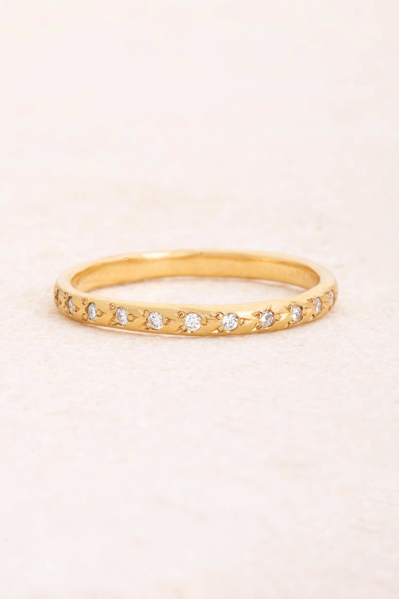 Flat lay of the Rosette ring with eleven flower-set white diamonds in textured recycled yellow gold