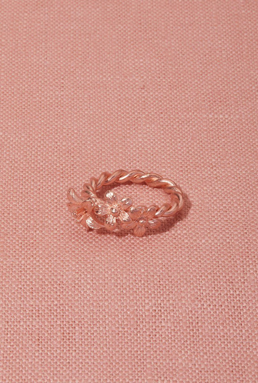 Garland ring in rose gold on pink linen flatly Garland ring is three wildflowers set on a twisted vine ring band.