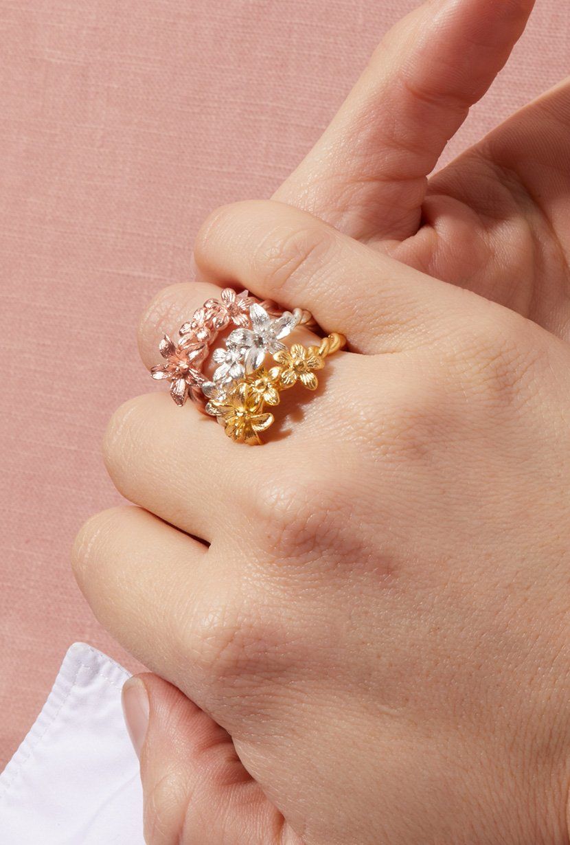 Sterling silver, yellow gold and rose gold garland rings stack on a models hand. Wildflowers entwined on a vine