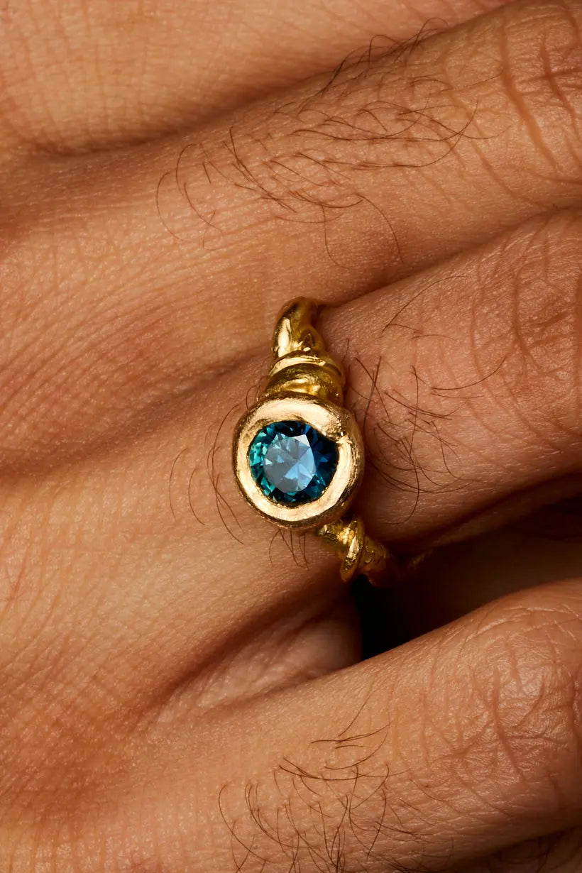 Close-up on models hand of sapphire set within curling vine-inspired gold band