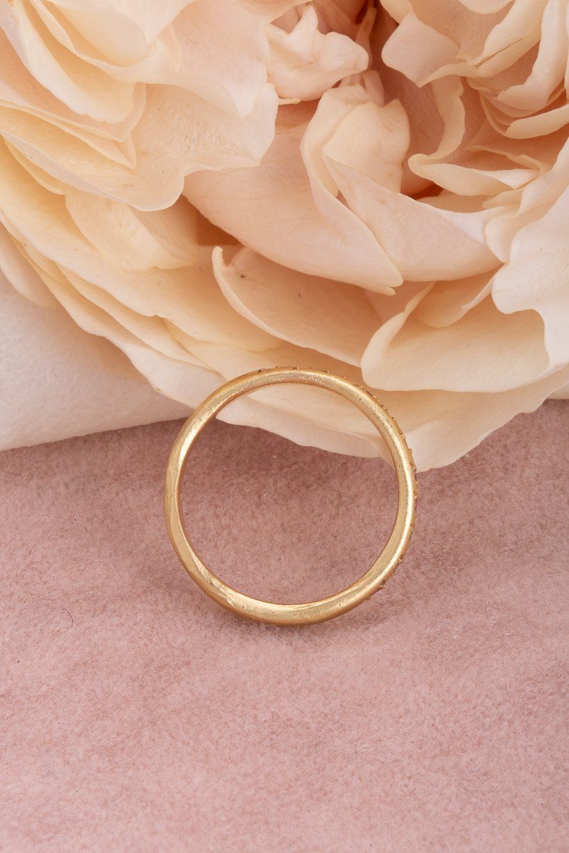 Side view of Rosette Ring in yellow gold with vivid pink sapphires on textured fabric with a rose