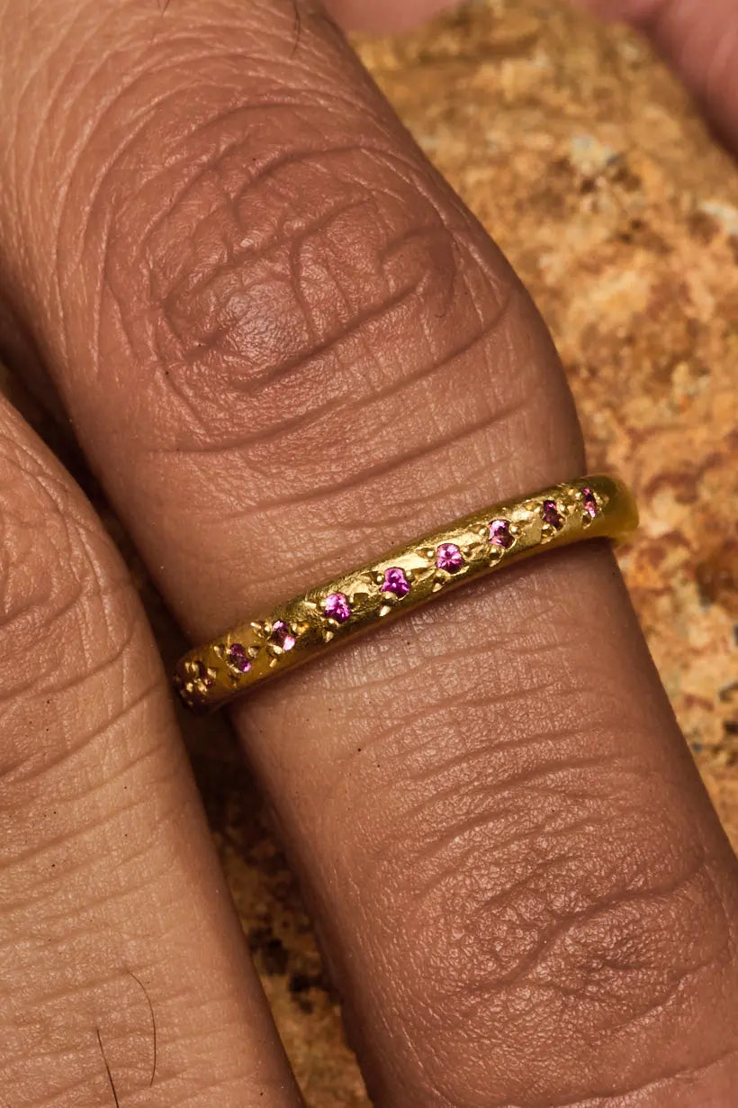 The Rosette Ring stacked with two plain gold bands on a model’s hand, softly lit