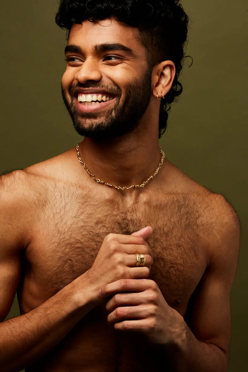 Model wears golden vine necklace and a stack of golden rings.