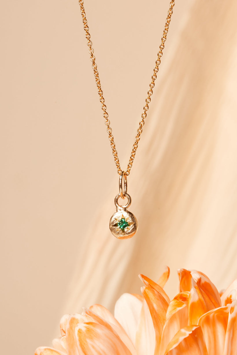 Close-up of emerald birthstone charm on gold chain