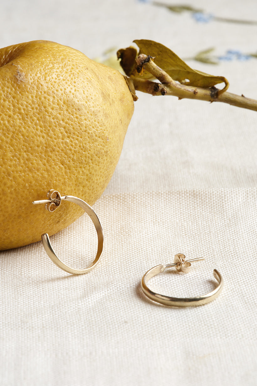 Gold hoop earrings on a white surface with a lemon and branch in the background