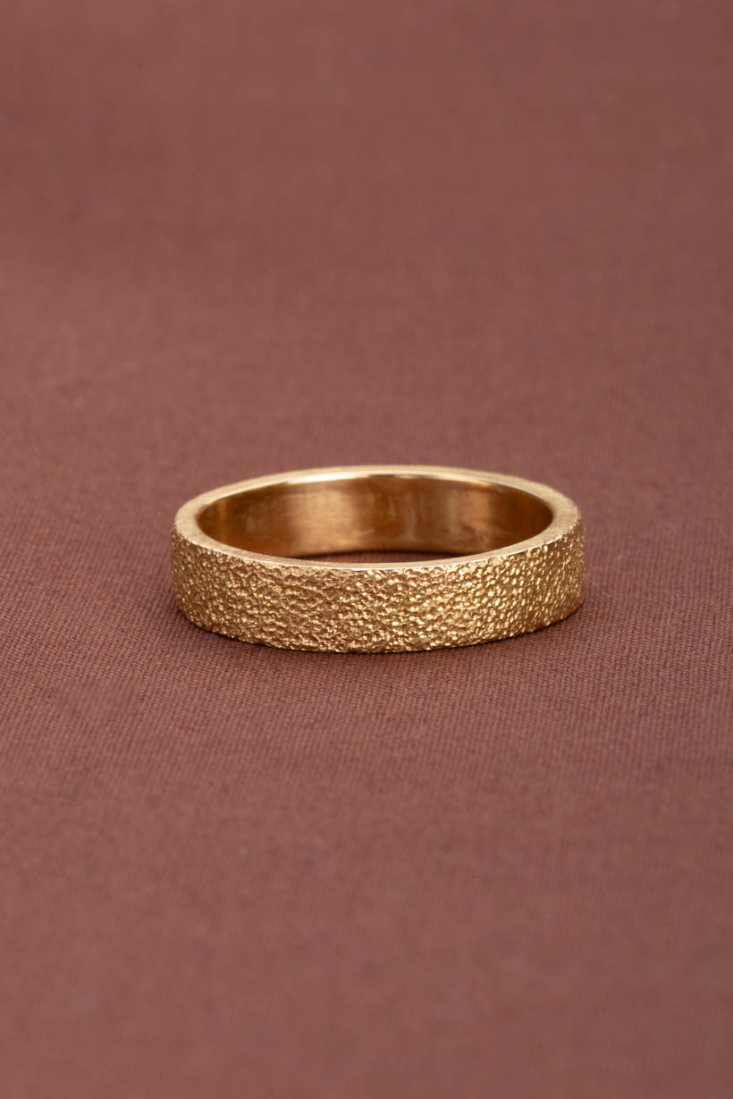 Gold ring with a textured surface on a brown background. Citrus ring highly textured unique wedding band. 