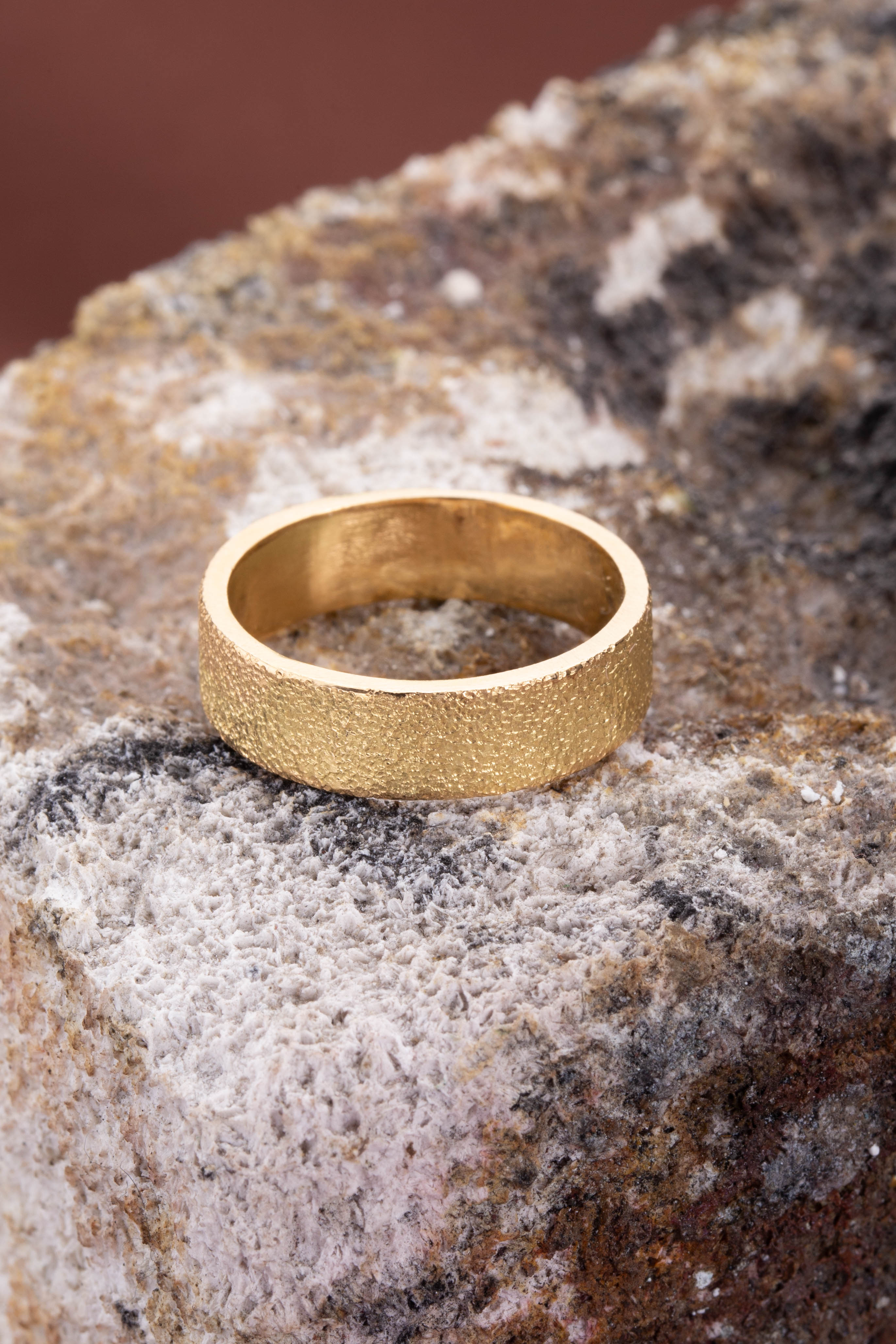 Gold ring on a textured stone surface. Unique, highly textured citrus ring. Wide gold wedding band. 