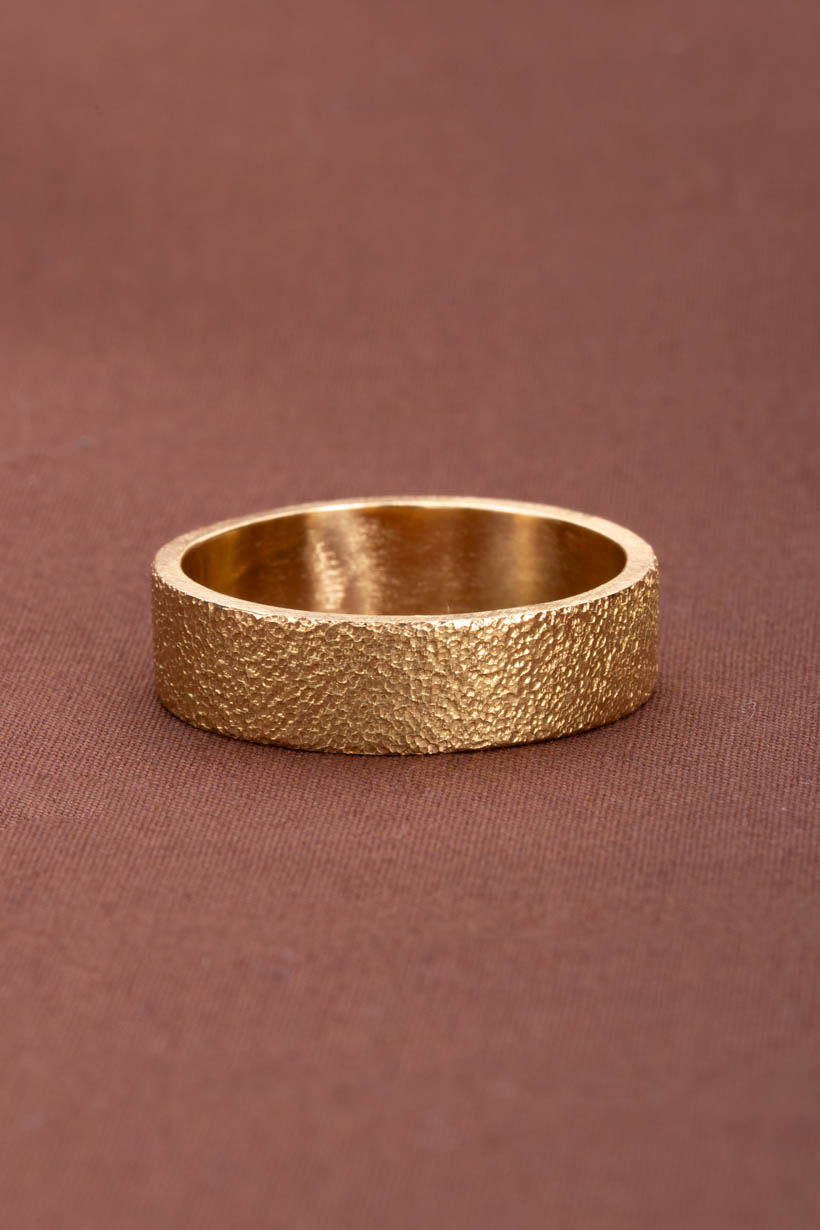 Gold ring with a textured surface on a brown background. Textured, organic wedding ring.