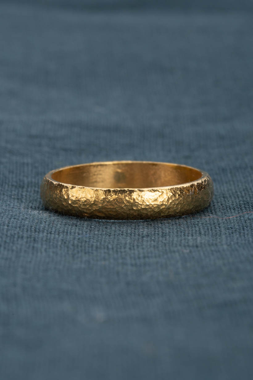 Moraine ring in gold. softly dappled textured gold wedding ring sitting on green fabric
