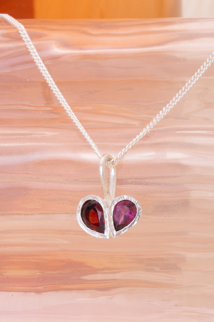 Heart-shaped pendant with red gemstone on a white chain against a beige background