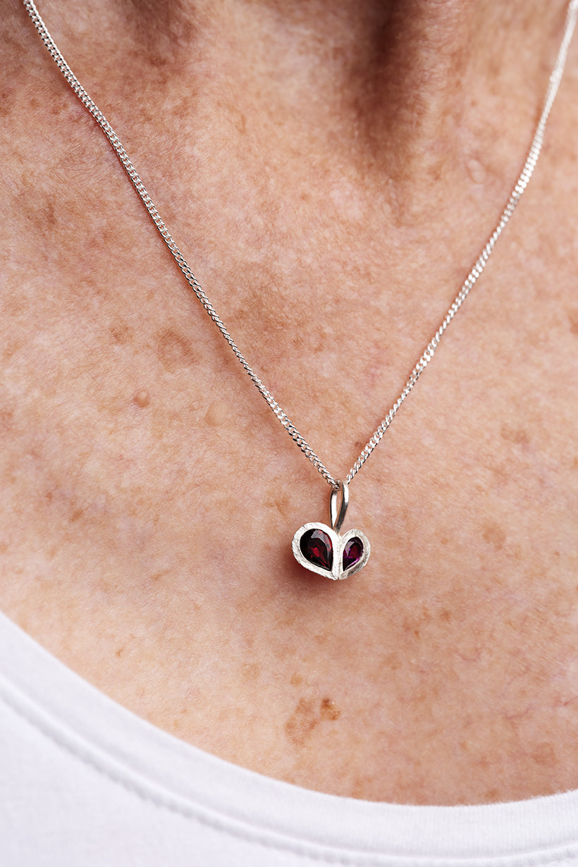 Heart-shaped pendant necklace with red stones on a person's neck