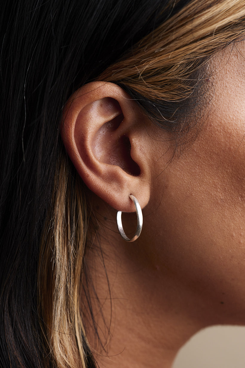 Close-up of an ear wearing a silver hoop earring with dark hair and skin.
