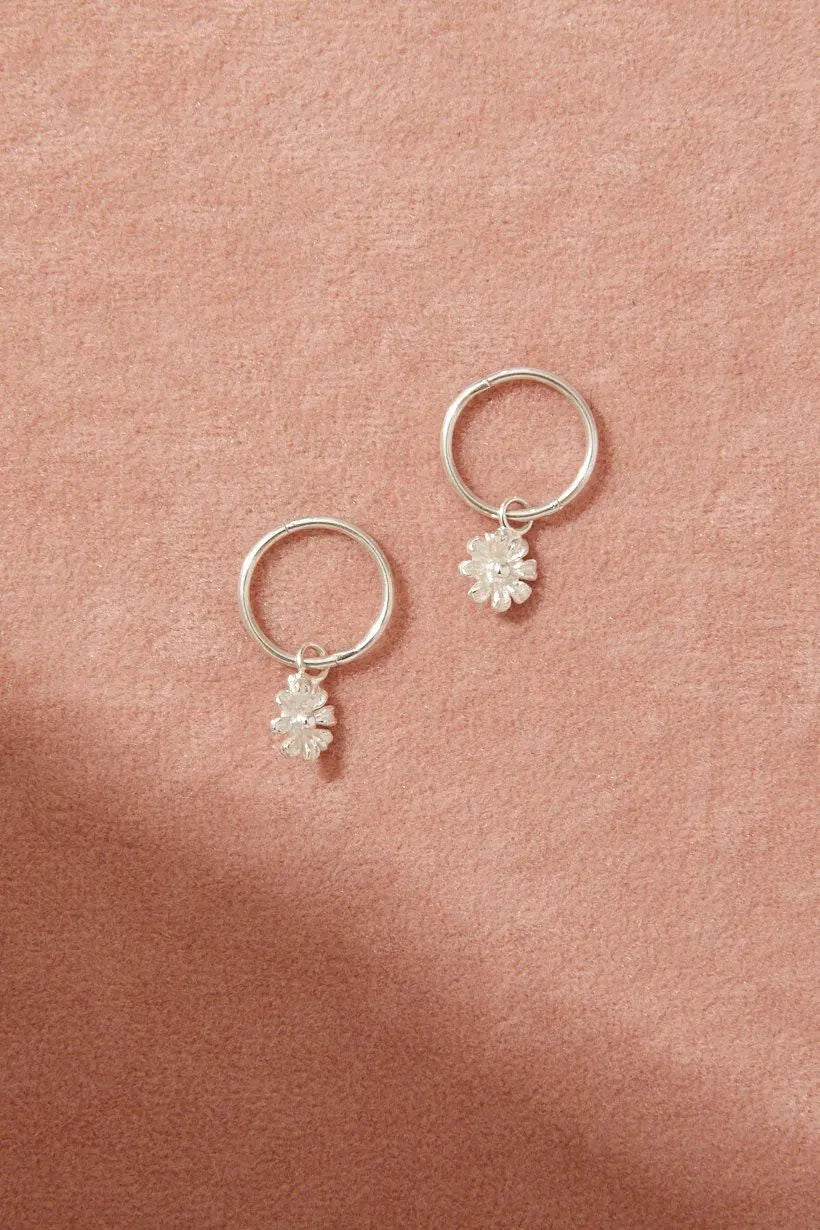 Flatlay of Daisy Sleepers on a pale pink fabric background – showcasing daisy details and fine silver finish