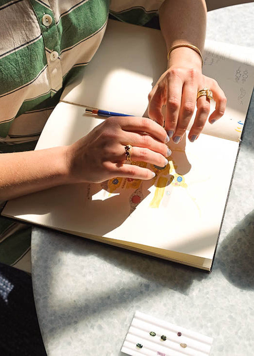 Person working on jewelry design with tools and materials on a table.
