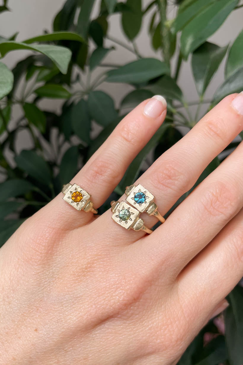 Model’s hand stacked with three Dawn Signet rings in gold and silver, featuring pink sapphire, green sapphire, and teal topaz gemstones.