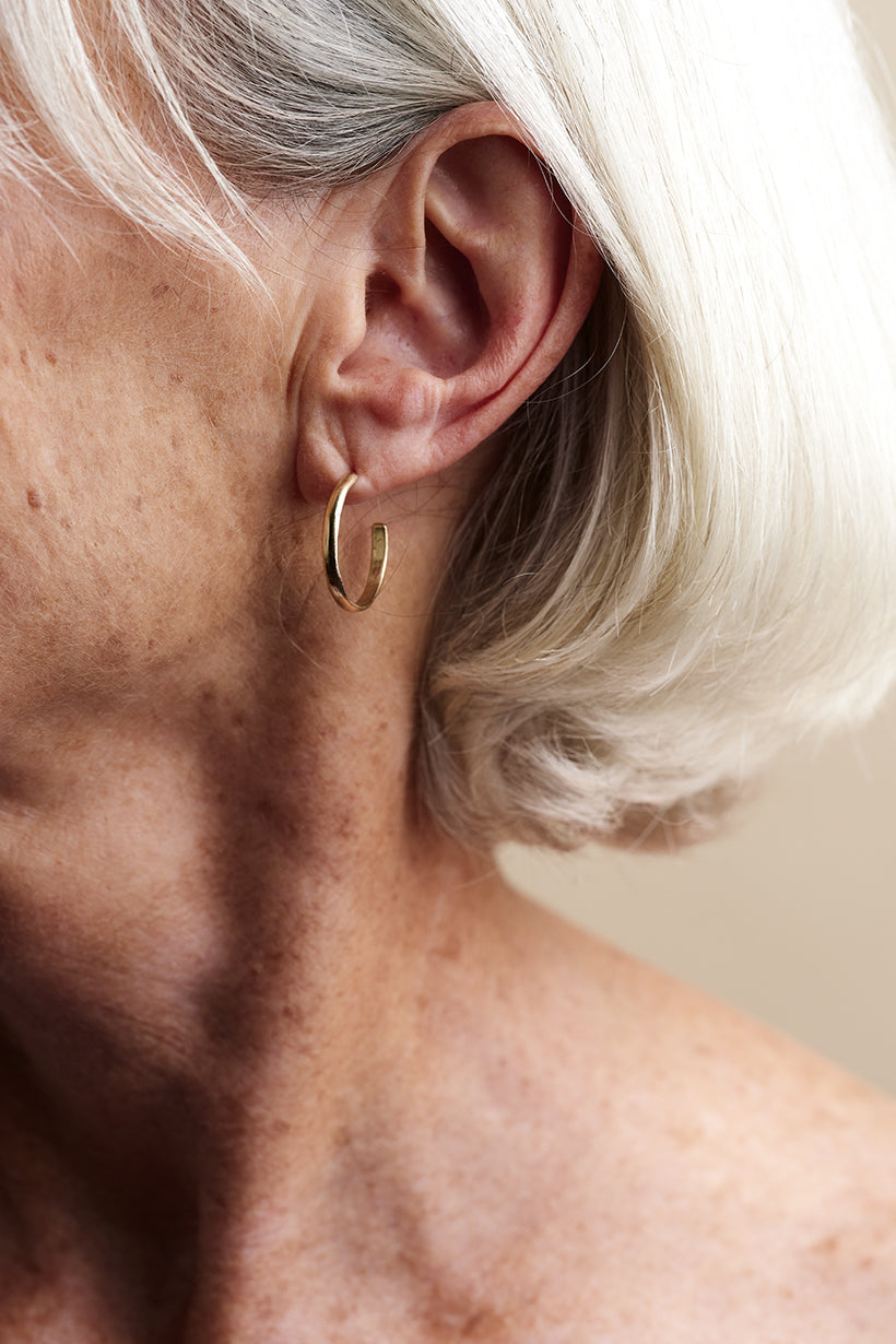 Close-up of an ear wearing a gold hoop earring with a neutral background
