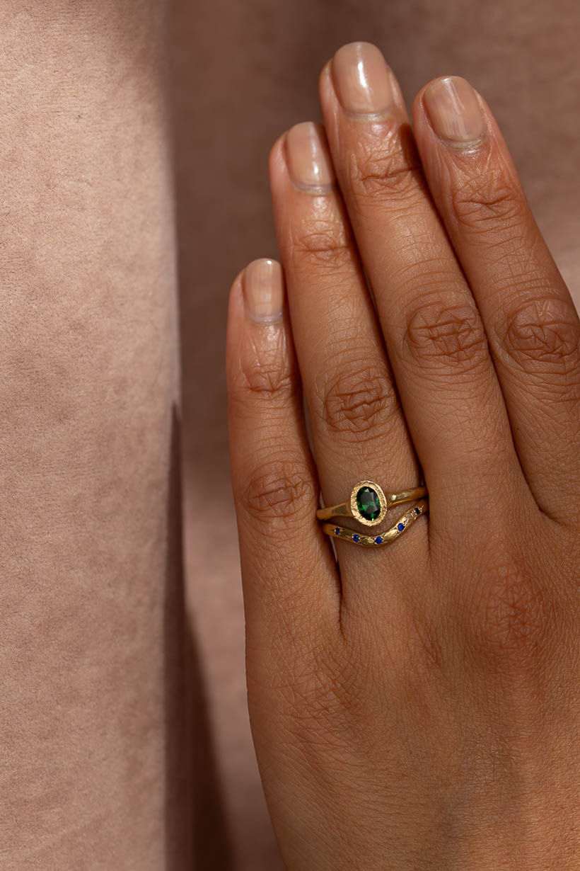 The Bower ring with green Australian sapphire low profile engagement ring in textured recycled gold stacked with the rosette ring, a curved wedding ring with 5 Australian blue sapphires handmade in Melbourne