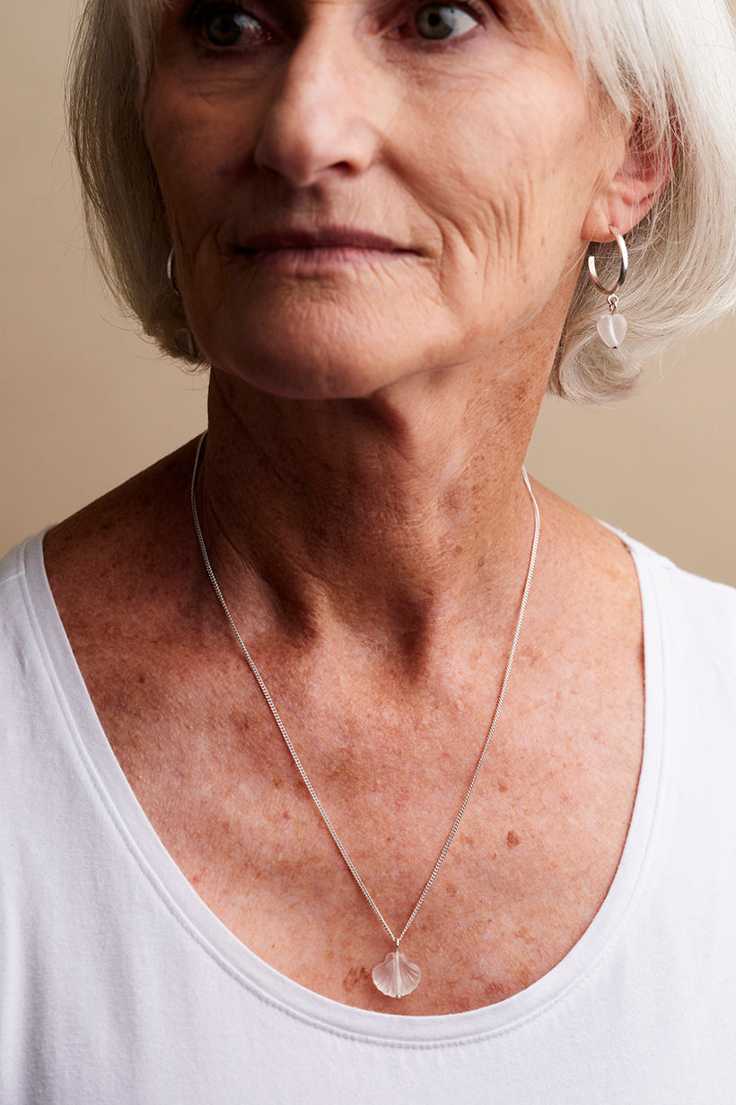 Woman wearing a necklace with a clear pendant against a neutral background