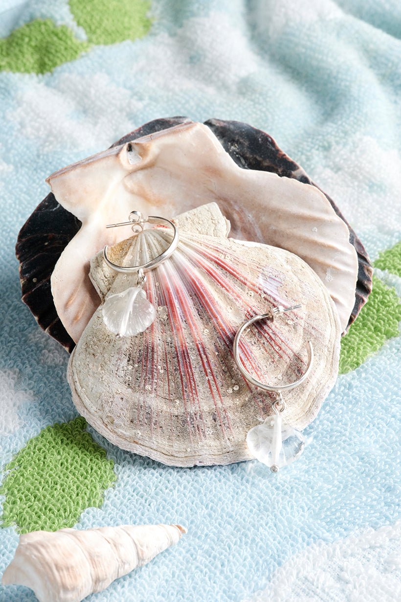 Glass shell on sterling silver hoops on a textured surface