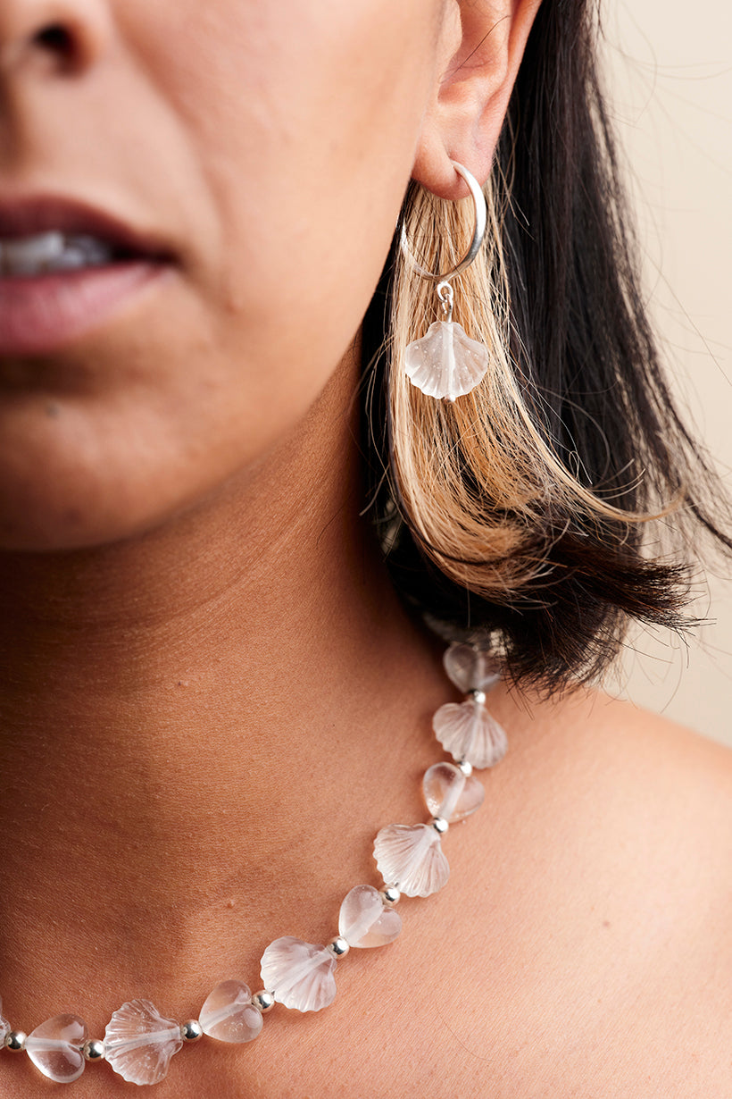 Close-up of a person wearing a necklace and earrings with a neutral background