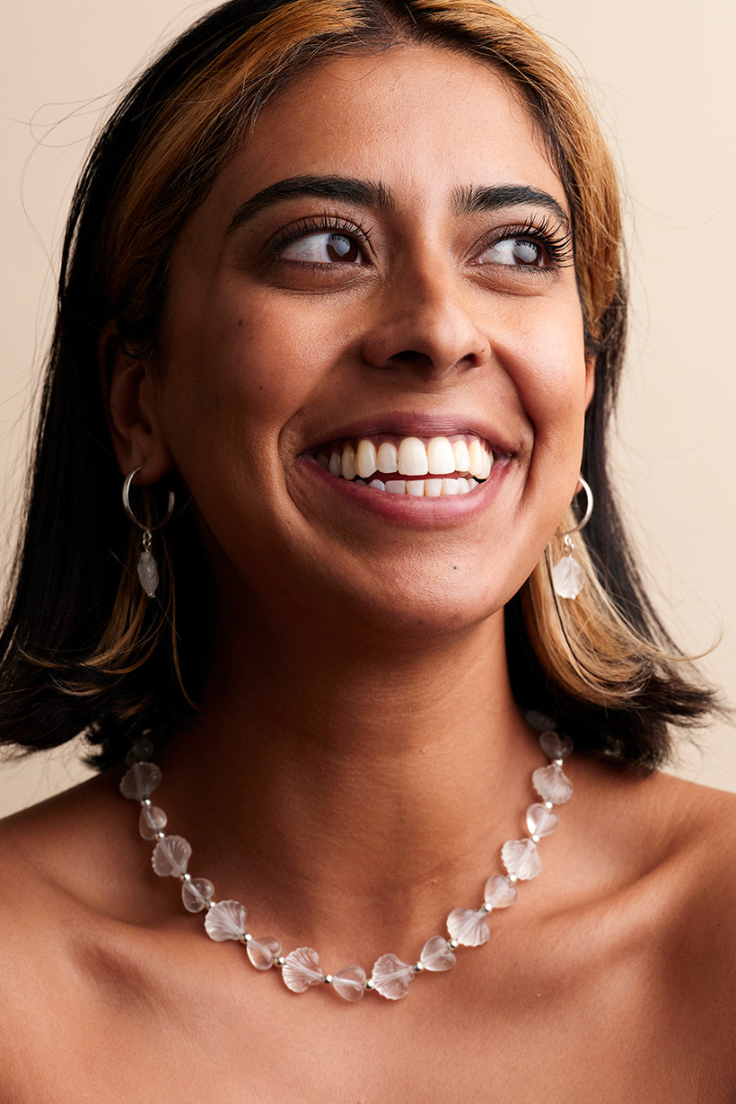 Woman wearing Daydream necklace, handmade glass shells and hearts, with a neutral background