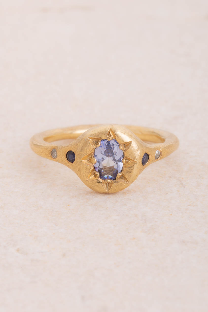 Monet's Garden low-profile engagement ring with a pale blue Ceylon sapphire centre stone, flanked by two dark blue Australian sapphires and two flush-set white diamonds, handmade in Melbourne from recycled gold, front view on limestone