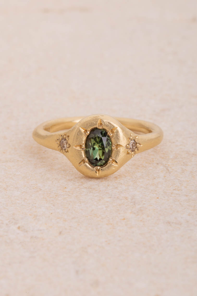 Monet’s Garden ring with an oval green Australian sapphire and two champagne diamonds in flower settings, handmade in recycled gold, front view on limestone